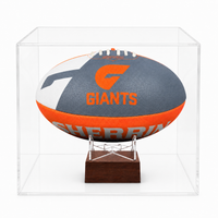 A Sherrin football displayed inside a clear acrylic display case on a small wooden stand. The ball is gray, orange, and white with the text 'GIANTS' and a large 'G' logo,