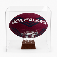 A maroon and navy Sea Eagles rugby ball displayed inside a clear acrylic cube case on a wooden stand, photographed against a clean white background.