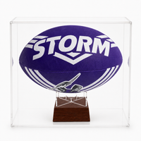 A purple and white Storm NRL jersey rugby ball mounted inside a clear acrylic display case on a dark wood stand, photographed against a white background.