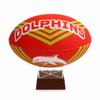 A red rugby ball with 'DOLPHINS' and a dolphin logo, displayed on a clear acrylic stand with a dark wooden base against a white background.