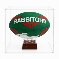 A green and red Rabbitohs rugby ball displayed inside a clear acrylic cube case on a dark wood stand, photographed against a white background.