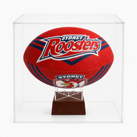 A red Sydney Roosters rugby ball urn displayed inside a clear acrylic cube stand on a dark wooden base, photographed against a light gray studio background.