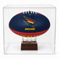 A navy blue and red Adelaide Crows football displayed inside a clear acrylic display case on a wooden stand.