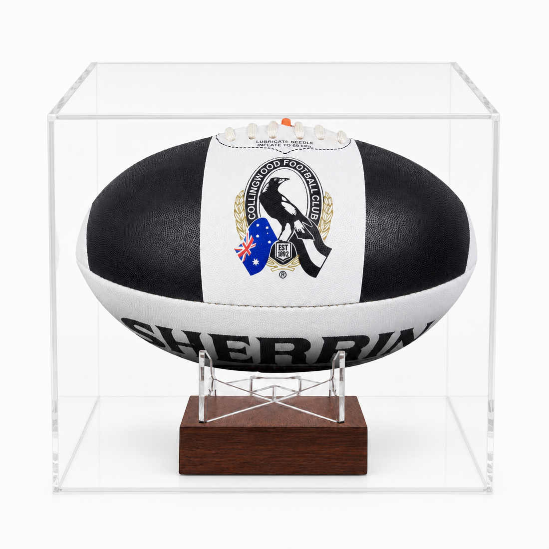 A black and white AFL ball with a Magpies logo, displayed inside a clear acrylic case on a wooden stand.