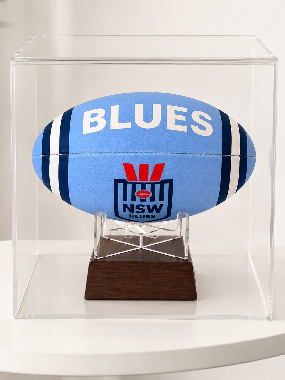 A light blue NSW Blues rugby ball displayed inside a clear acrylic case on a dark wood stand, set against a clean white background.