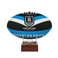 A custom Port Adelaide Football Club rugby ball  urn with a black, blue, and white striped design, displayed on a clear acrylic stand with a dark brown wooden base against a white background.