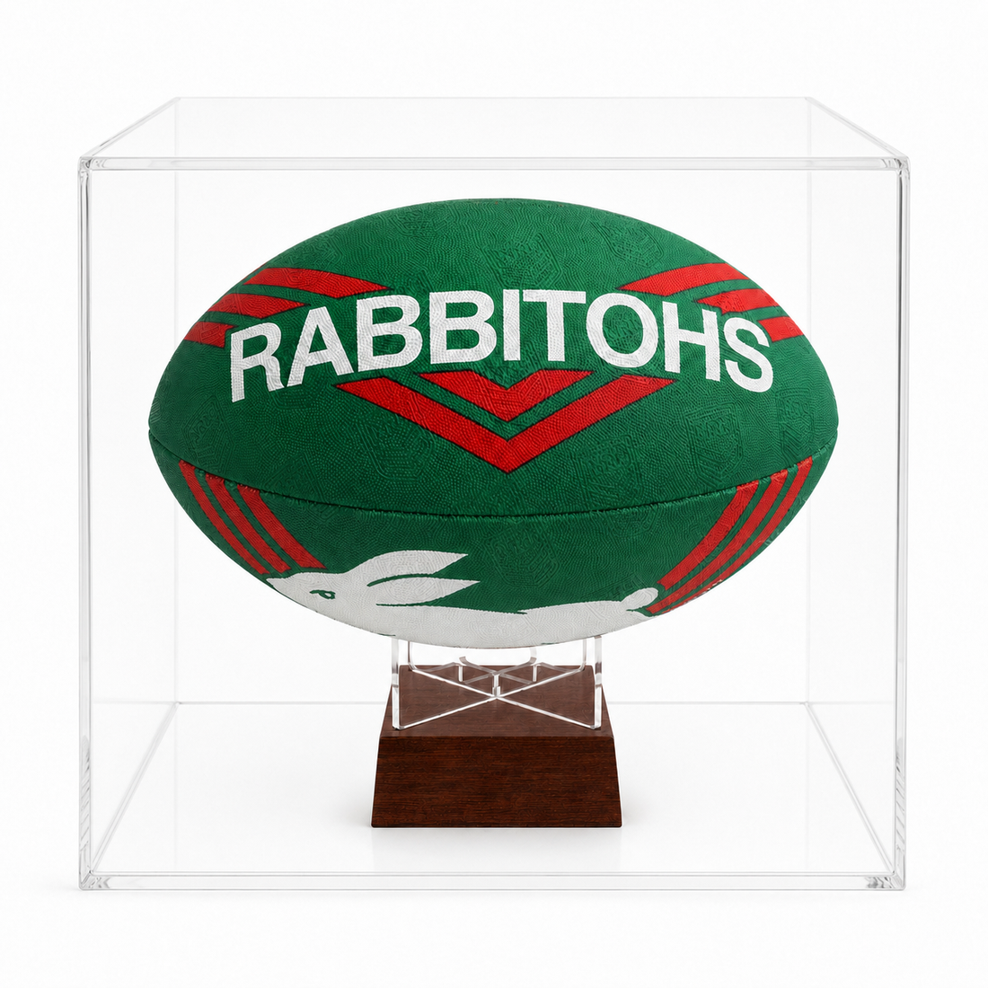 A green and red Rabbitohs rugby ball displayed inside a clear acrylic cube case on a dark wood stand, photographed against a white background.