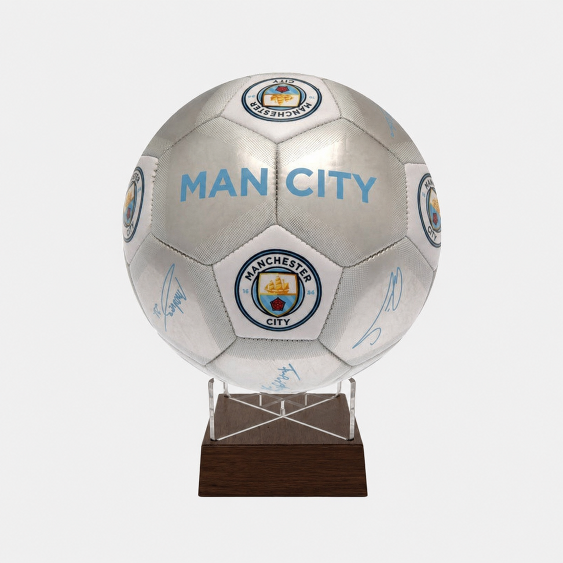 A Manchester City soccer ball signed by players, mounted on a clear acrylic stand with a dark brown wooden base, shown against a light gray background.