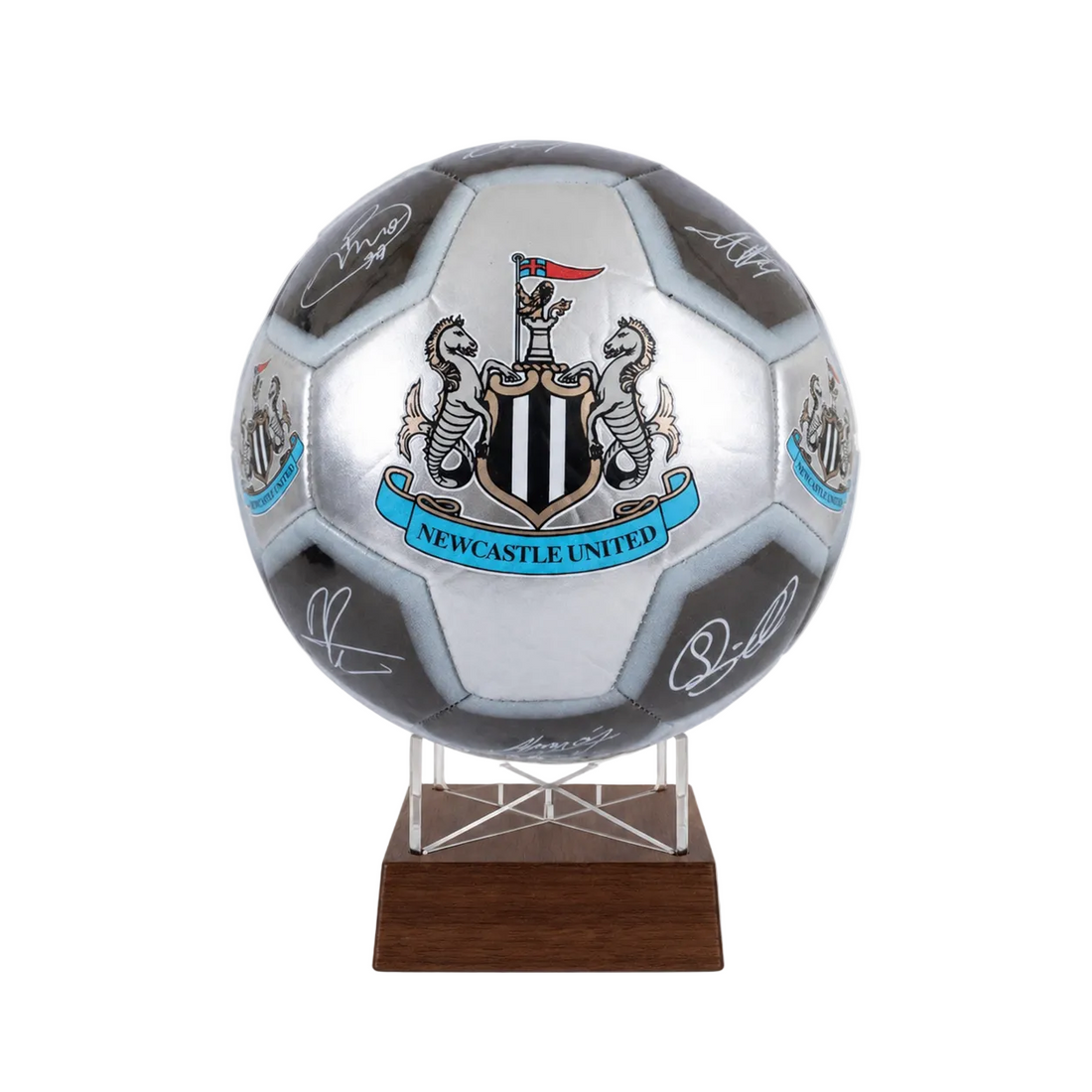 A silver and black soccer ball featuring the Newcastle United crest and multiple player signatures, displayed on a clear stand with a dark wood base against a light gray background.